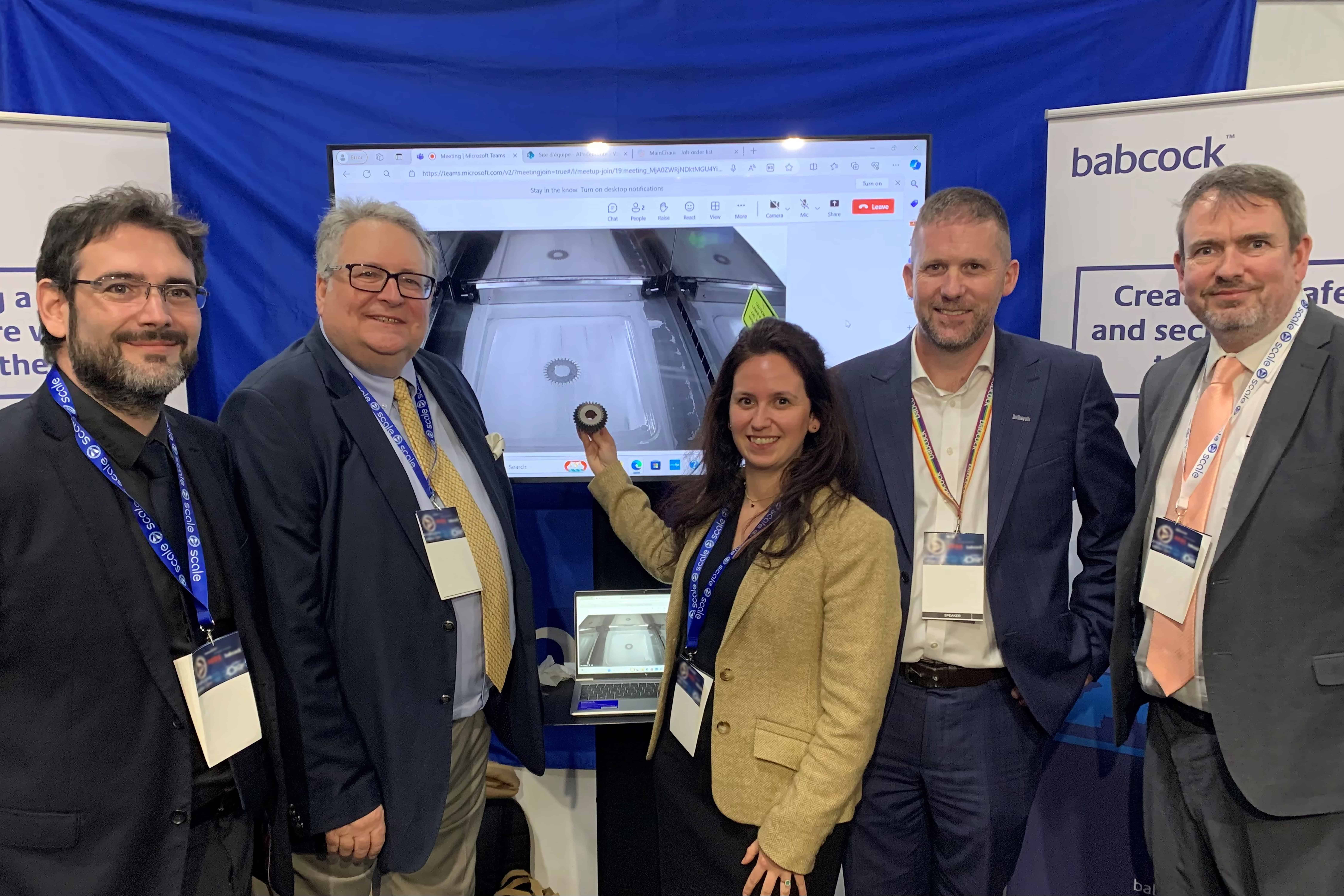Photo of Babcock collaborative team at Defence Procurement Research Technology Exportability Conference displaying the transmission gear which was remotely manufactured at the event