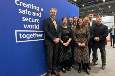 A group of people at the IT2TEC conference standing in front of a blue backdrop with the words 'Creating a safe and secure world, together' on it.