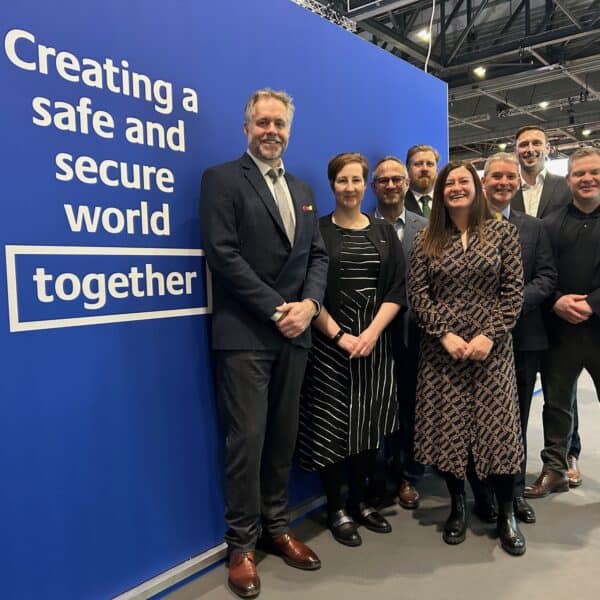 A group of people at the IT2TEC conference standing in front of a blue backdrop with the words 'Creating a safe and secure world, together' on it.