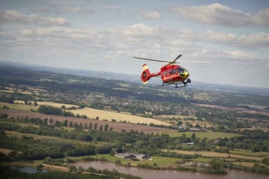 Midlands Air Ambulance red helicopter flying over countryside