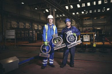 Two Babcock employees in blue overalls holding the crests for each of the three Type 31 frigates - Active, Venturer and Formidable