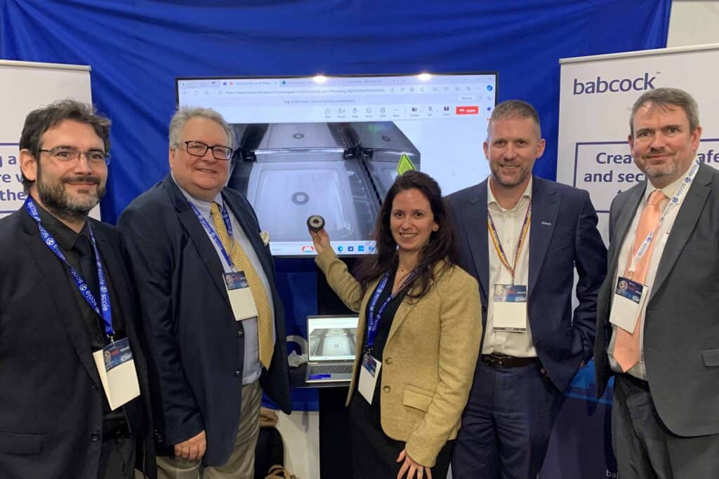 Photo of Babcock collaborative team at Defence Procurement Research Technology Exportability Conference displaying the transmission gear which was remotely manufactured at the event