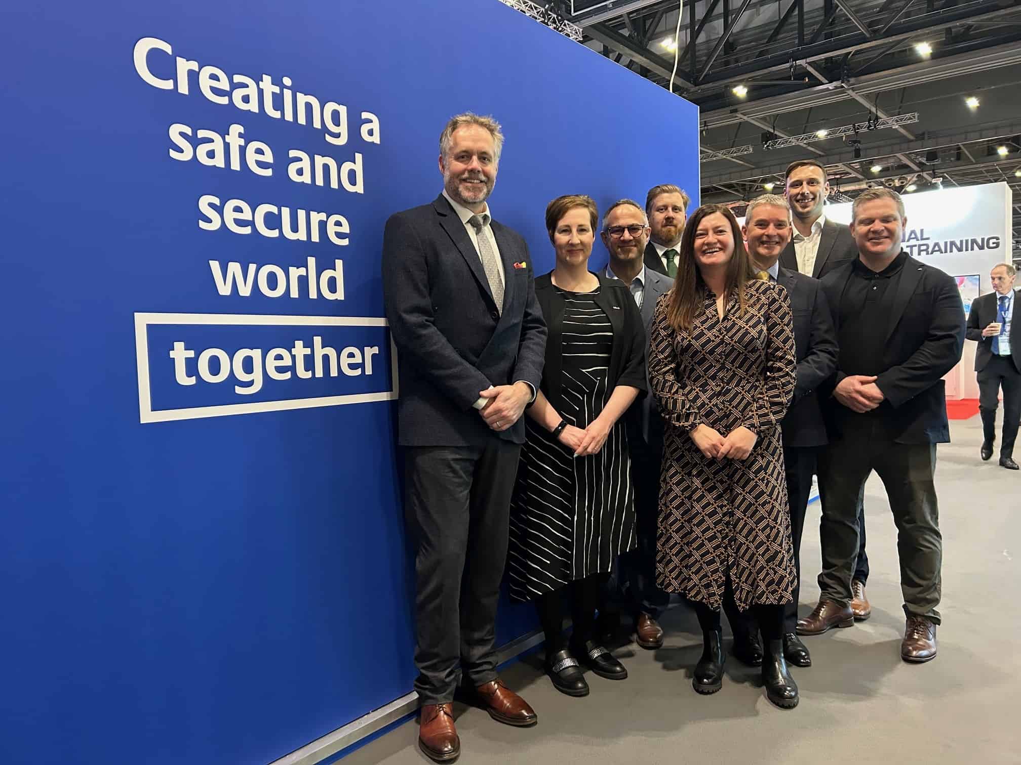 A group of people at the IT2TEC conference standing in front of a blue backdrop with the words 'Creating a safe and secure world