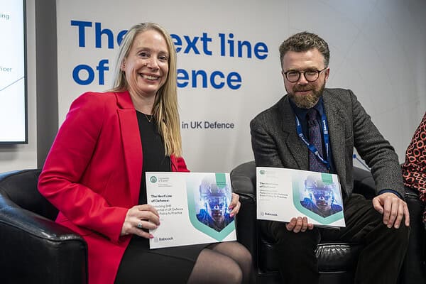 Two professionals seated holding reports titled 'The Next Line of Defence'