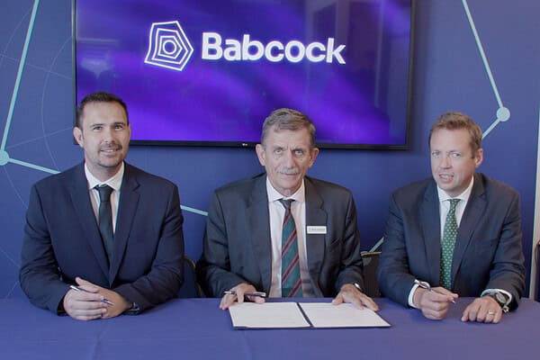 Representatives from ACUA Ocean Technologies, Babcock and Frankenburg with signed Memorandum of Understanding, in front of a blue Babcock branded background